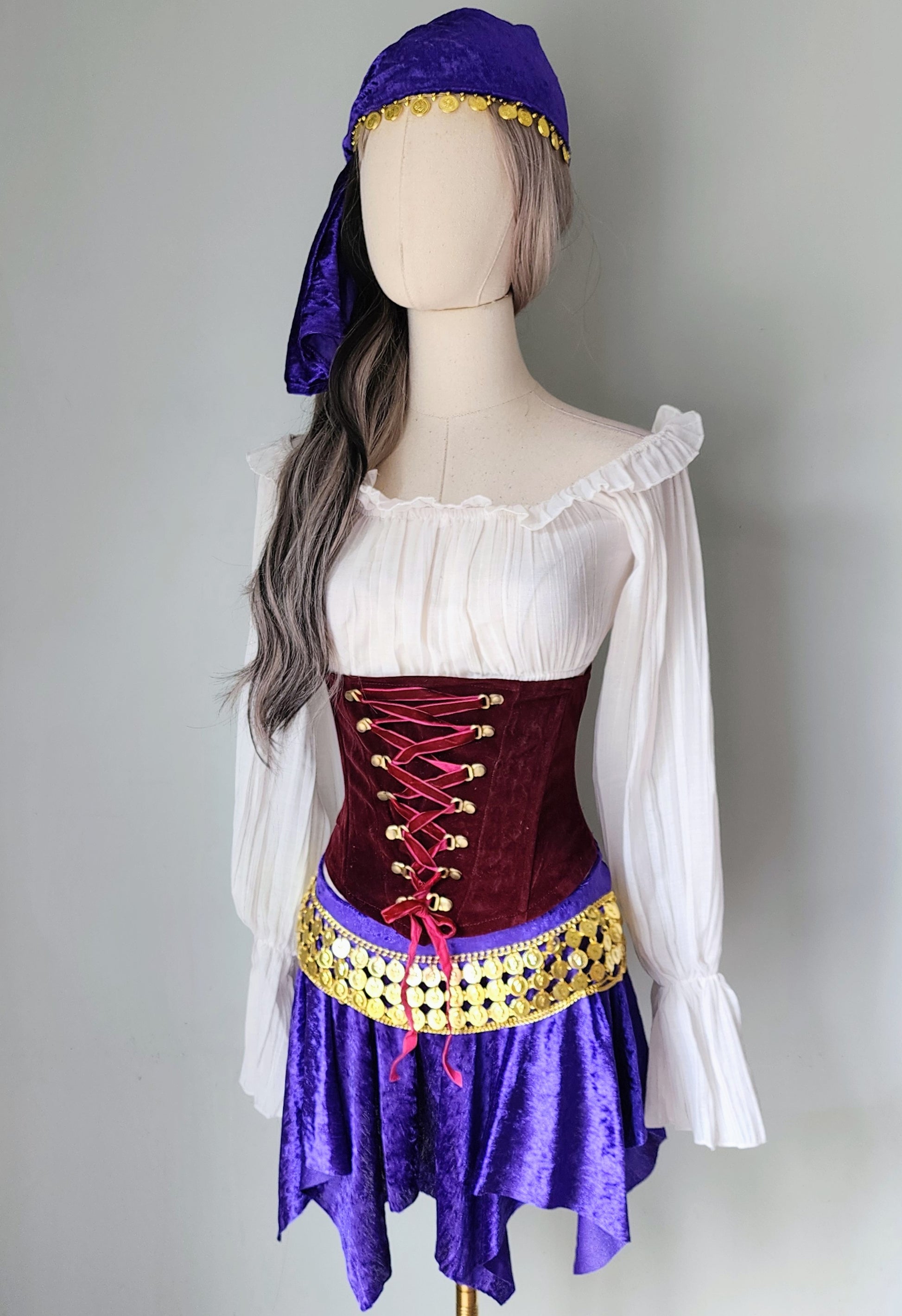 Mannequin wearing a costume with a white top, red corset, purple skirt, and purple headscarf on a gray background.